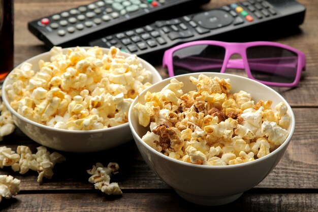 Palomitas de maíz, gafas 3D y control remoto de TV en una mesa de madera marrón, concepto de ver películas en casa.