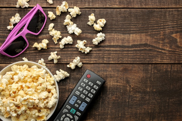 Palomitas de maíz, gafas 3D y control remoto de TV sobre un fondo de madera marrón. concepto de ver películas en casa. vista desde arriba