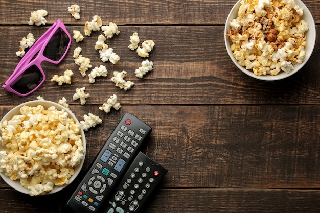 Palomitas de maíz, gafas 3D y control remoto de TV sobre un fondo de madera marrón. concepto de ver películas en casa. vista desde arriba