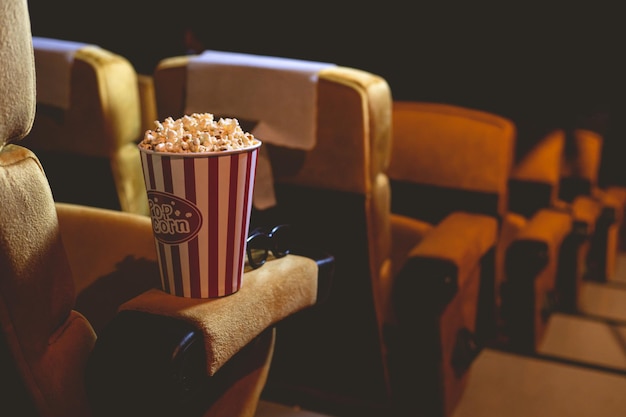 Palomitas de maíz y gafas 3d en un sillón amarillo en el cine con espacio de copia.