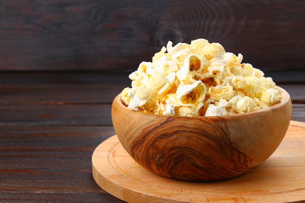 Palomitas de maíz saladas en un cuenco de madera en una tabla de madera.