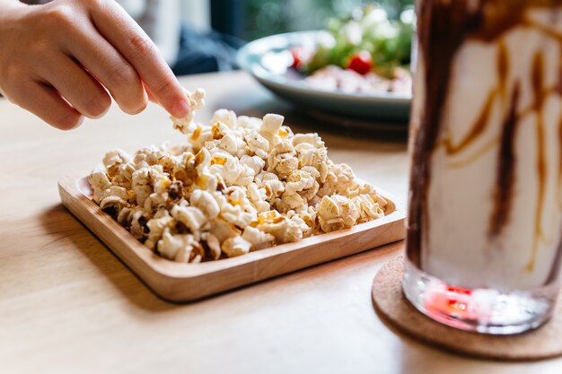 Las palomitas de maíz saladas con la selección de la mano sirvieron en placa de madera cuadrada en la tabla de madera.