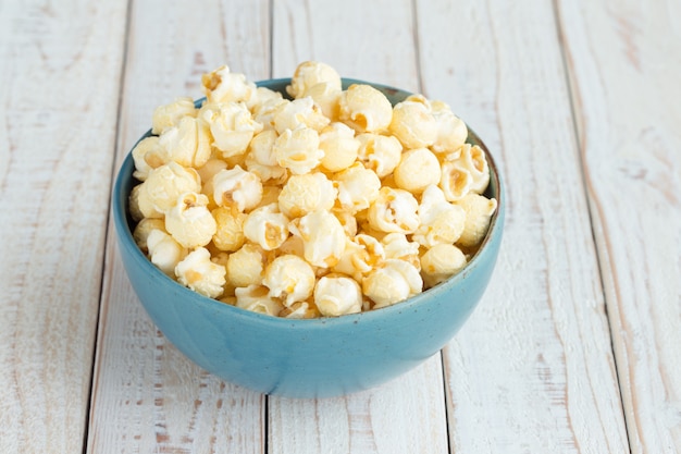 Palomitas de maíz en taza azul sobre mesa de madera blanca