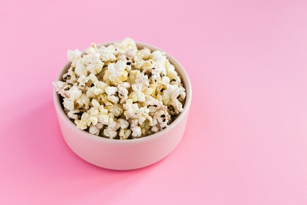 Palomitas de maíz en un tazón rosa sobre fondo rosa