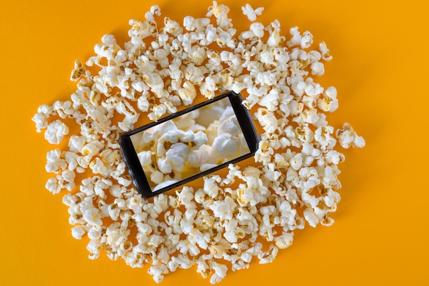 Palomitas de maíz y teléfono inteligente en la vista superior de fondo naranja