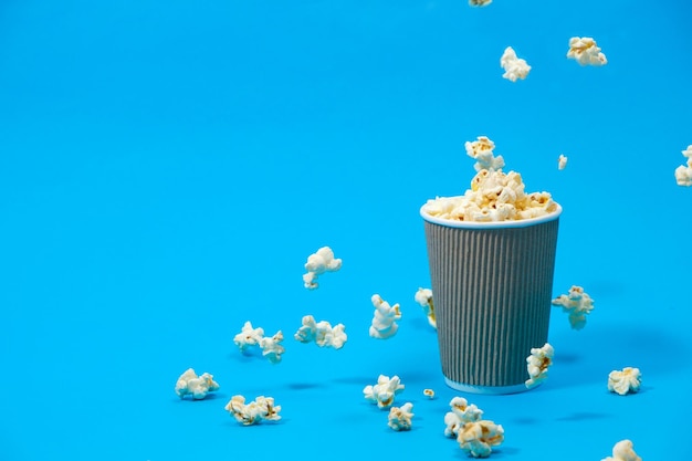 Las palomitas de maíz se vierten en un vaso de papel marrón sobre un fondo azul.