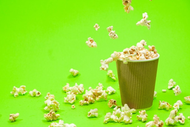 Las palomitas de maíz se vierten en un vaso de papel marrón sobre un fondo verde