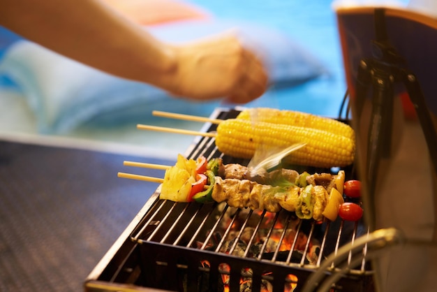 Palos de barbacoa en la estufa en el fondo de la piscina borrosa con la mano borrosa en movimiento