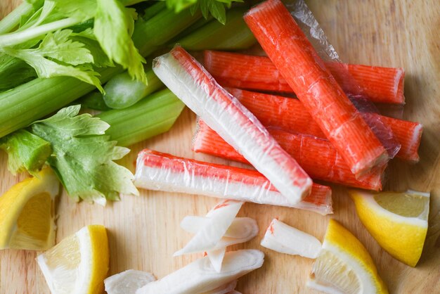 Foto palos de cangrejo con limón y verduras frescas de apio en un plato de madera