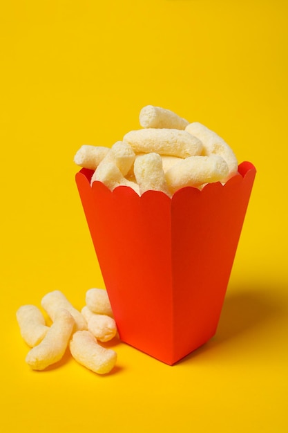 Palos de maíz dulce en taza de papel rojo sobre fondo amarillo