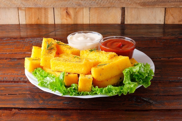 Palos de polenta fritos en plato de cerámica blanca sobre mesa de madera rústica