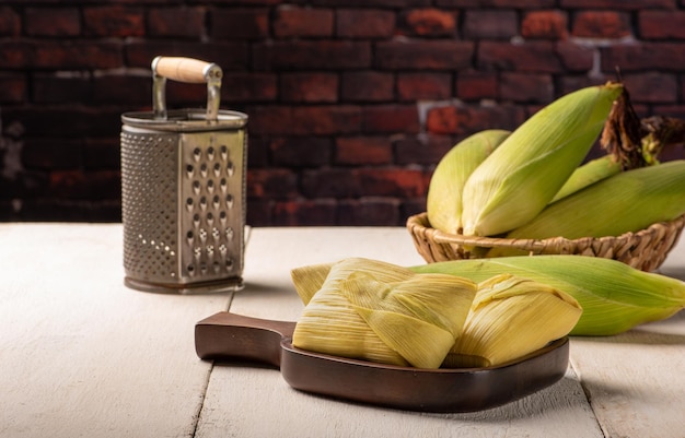 Foto pamonha de lanche de milho brasileiro e milho verde dispostos em uma mesa de madeira rústica branca foco seletivo