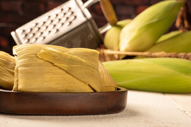 Pamonha de lanche de milho brasileiro e milho verde dispostos em uma mesa de madeira rústica branca foco seletivo