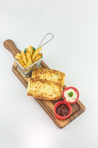 Pan de ajo con queso y papas fritas en canasta con salsa de tomate y salsa sobre fondo blanco.