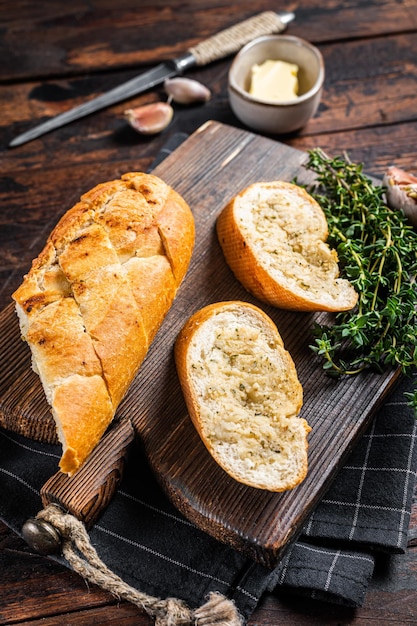 Pan de ajo tostado con hierbas y mantequilla sobre tabla de cortar de madera. Fondo de madera. Vista superior.