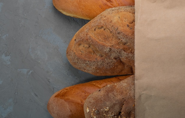 Pan y baguette recién horneados en una bolsa de papel sobre un fondo de textura gris.