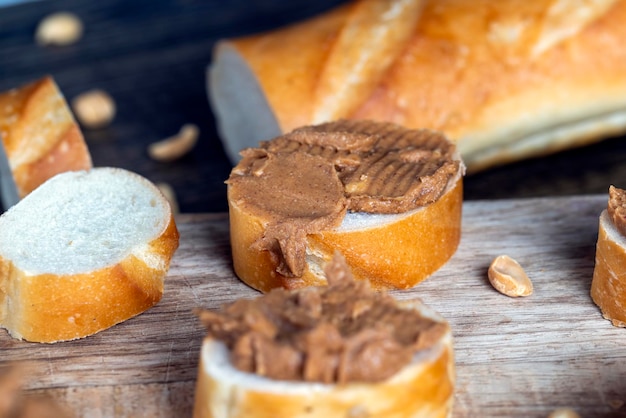 Pan blanco rebanado con mantequilla de maní con mantequilla con trozos de maní triturado en una tabla de madera cortada en la cocina