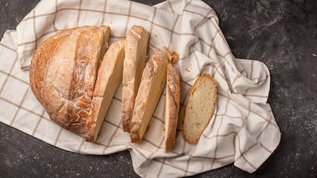 Pan blanco redondo cortado en muchos trozos, ubicado con una servilleta a cuadros blanca sobre negro