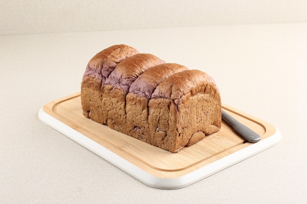 Pan de camote morado sobre tabla de cortar de bambú. Fondo limpio y fresco con espacio para copiar texto o publicidad