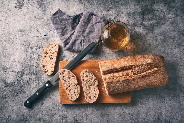 Pan casero cortado en una tabla de madera junto con una botella de aceite de oliva virgen extra. Concepto tradicional de desayuno mediterráneo.