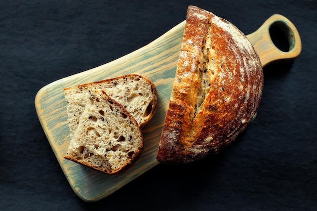 El pan casero fresco se encuentra en una tabla de cortar sobre un fondo oscuro Pan de masa fermentada francesa crujiente Productos horneados frescos con cereales con sus propias manos