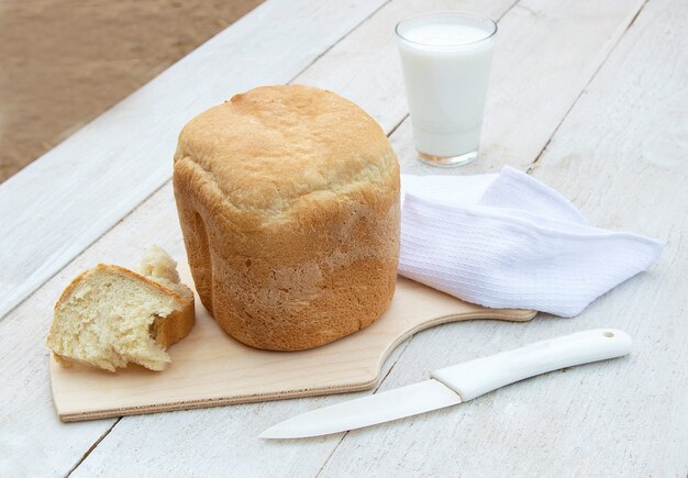 Pan casero fresco y un vaso de yogur orgánico casero natural sobre un fondo de madera blanca