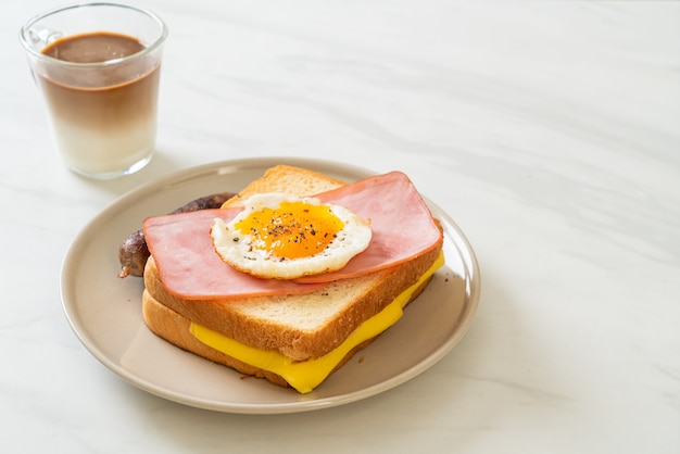 Pan casero con queso tostado, jamón y huevo frito con salchicha de cerdo y café para el desayuno.