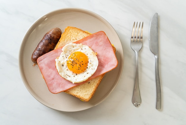 Pan casero con queso tostado, jamón y huevo frito con salchicha de cerdo para el desayuno.