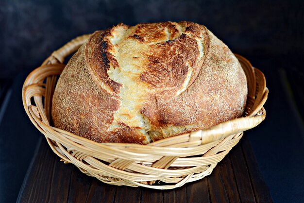 Pan casero recién horneado en una canasta hecha de trigo y harina integral sobre un fondo oscuro.