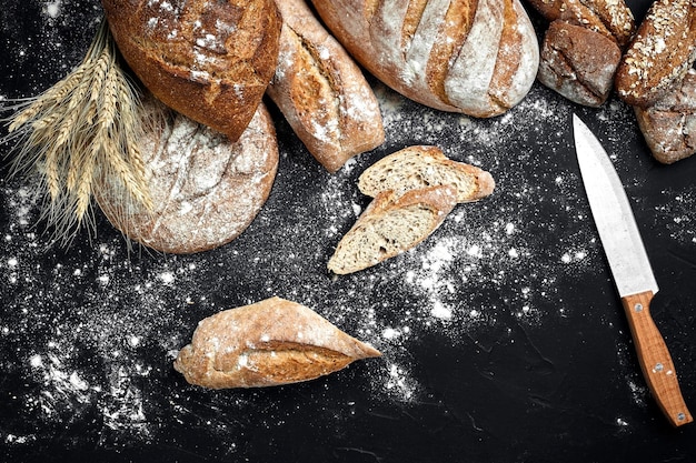 Pan de centeno casero espolvoreado con harina y varios granos y semillas sobre un fondo negro con espigas de trigo o centeno y avena