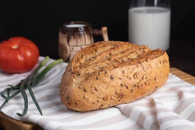 Pan de centeno casero fresco racimo de tomate cebolla taza de arcilla y una botella de leche en una tabla de cortar de madera