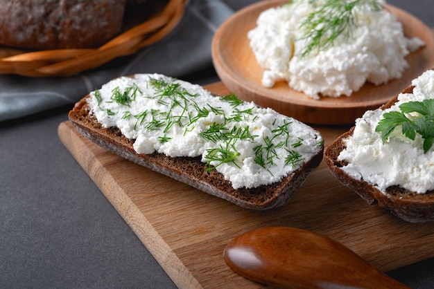 Pan de centeno casero en una tabla de cortar de madera con requesón ricotta y eneldo