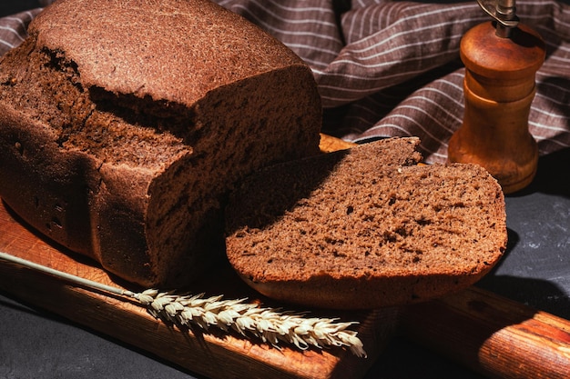 Pan de centeno marrón recién horneado en rodajas en una tabla de cortar de madera sobre fondo negro