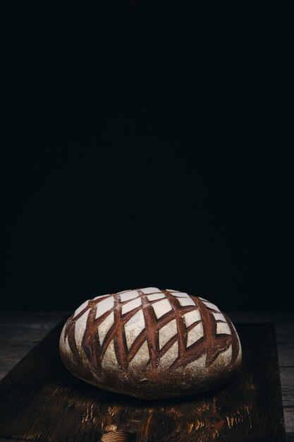 Pan de centeno negro espolvoreado con harina sobre fondo oscuro de madera rústica