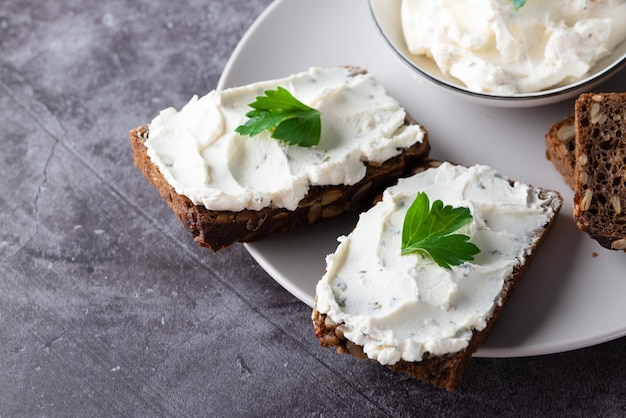 Pan de centeno con queso crema sobre mesa gris Pan integral de centeno con semillas