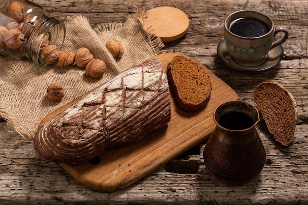 Pan de centeno en rodajas sobre una tabla, nueces de café y un turco para hacer café sobre una mesa de madera