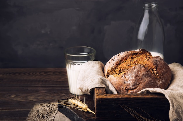 Pan de centeno rústico casero con semillas de cilantro y una botella de leche en la mesa de madera vieja.