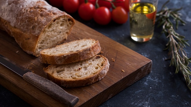 Pan ciabatta casero crujiente sobre tabla de cortar de madera con tomates y aceite de oliva. Pan fresco