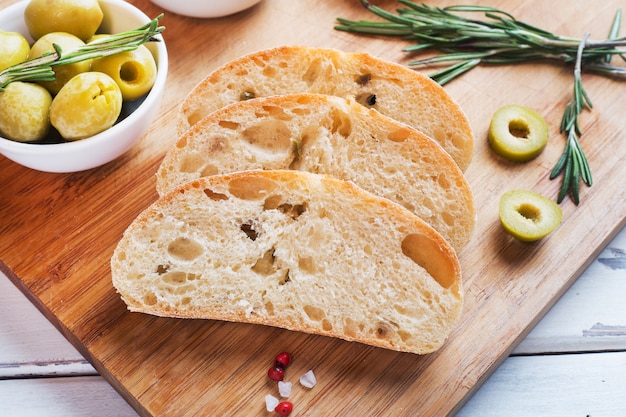 Pan ciabatta italiano con aceitunas y romero en una tabla de madera.