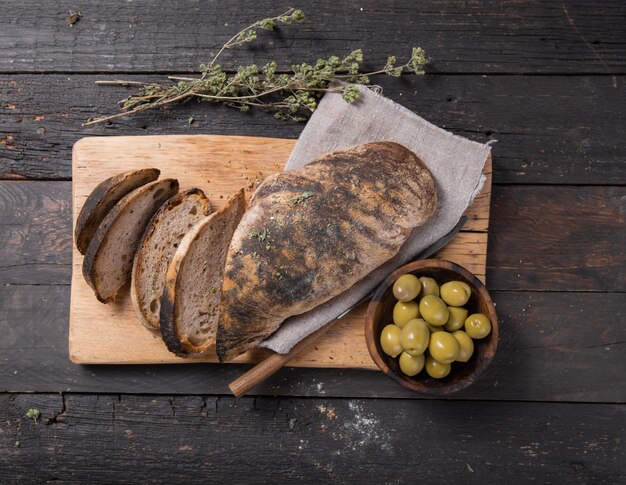 Pan ciabatta italiano fresco para levadura con hierbas, aceitunas sobre fondo de madera, vista superior, espacio de copia.