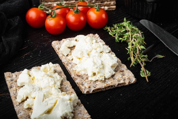 Pan crujiente de centeno fresco con queso crema, sobre fondo de mesa de madera negra