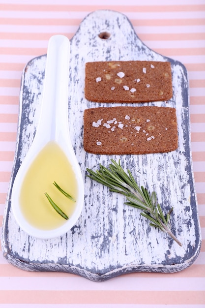 Pan crujiente con cuchara de sal de aceite y ramitas de romero en la tabla de cortar sobre fondo rayado