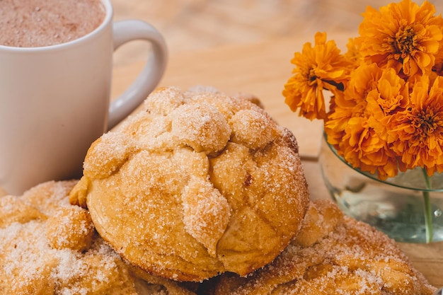 Pan de Muerto mit Zucker und einer Tasse Schokolade auf einem Brett mit Cempasúchil-Blüten.