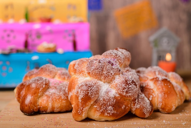 Pan de muertos auf Holztisch mit Altar im Hintergrund. Typisches Dessert zum Tag der Toten.