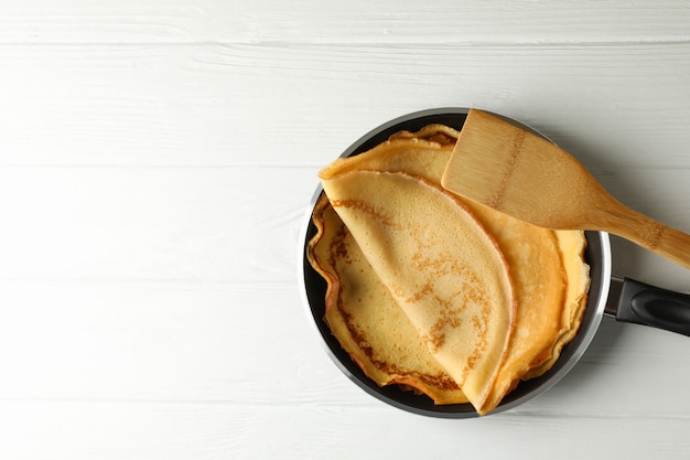 Pan con deliciosos panqueques finos y espátula sobre mesa de madera