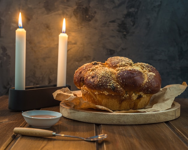 Foto pan dulce de jalá en un plato redondo arbolado en una mesa de madera marrón con miel y dos velas en la noche de shabat haciendo kidush