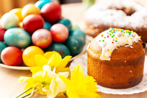 Pan dulce ortodoxo de Pascua, kulich, huevos de colores y un ramo de narcisos. Luz solar brillante. Desayuno tradicional de Pascua. Enfoque selectivo.