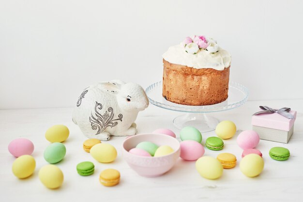 Pan dulce de Pascua, pastel de Pascua y huevos multicolores con tulipanes y un conejo blanco. Concepto de desayuno de vacaciones con espacio de copia.