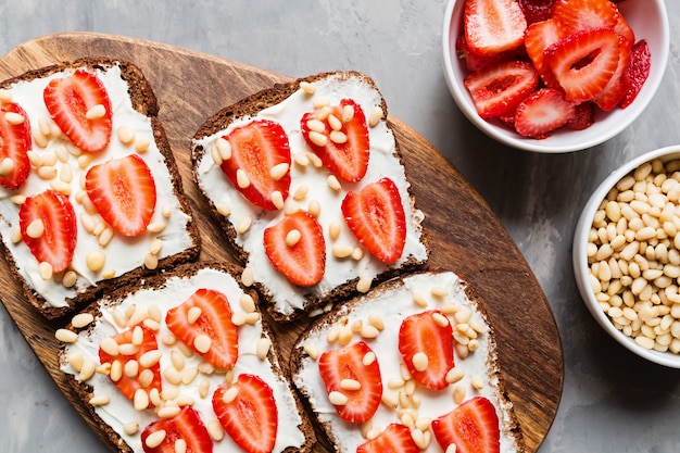 Pan con fresa, piñones y queso crema sobre fondo gris