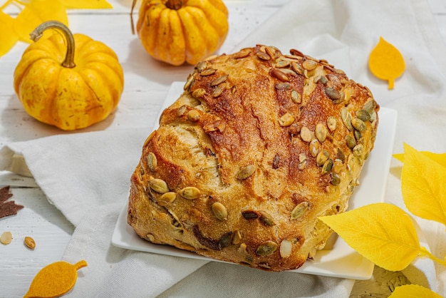 Foto pan fresco con semillas de calabaza concepto de horneado casero decoración de otoño hojas de otoño luz dura sombra oscura fondo de madera blanca de cerca